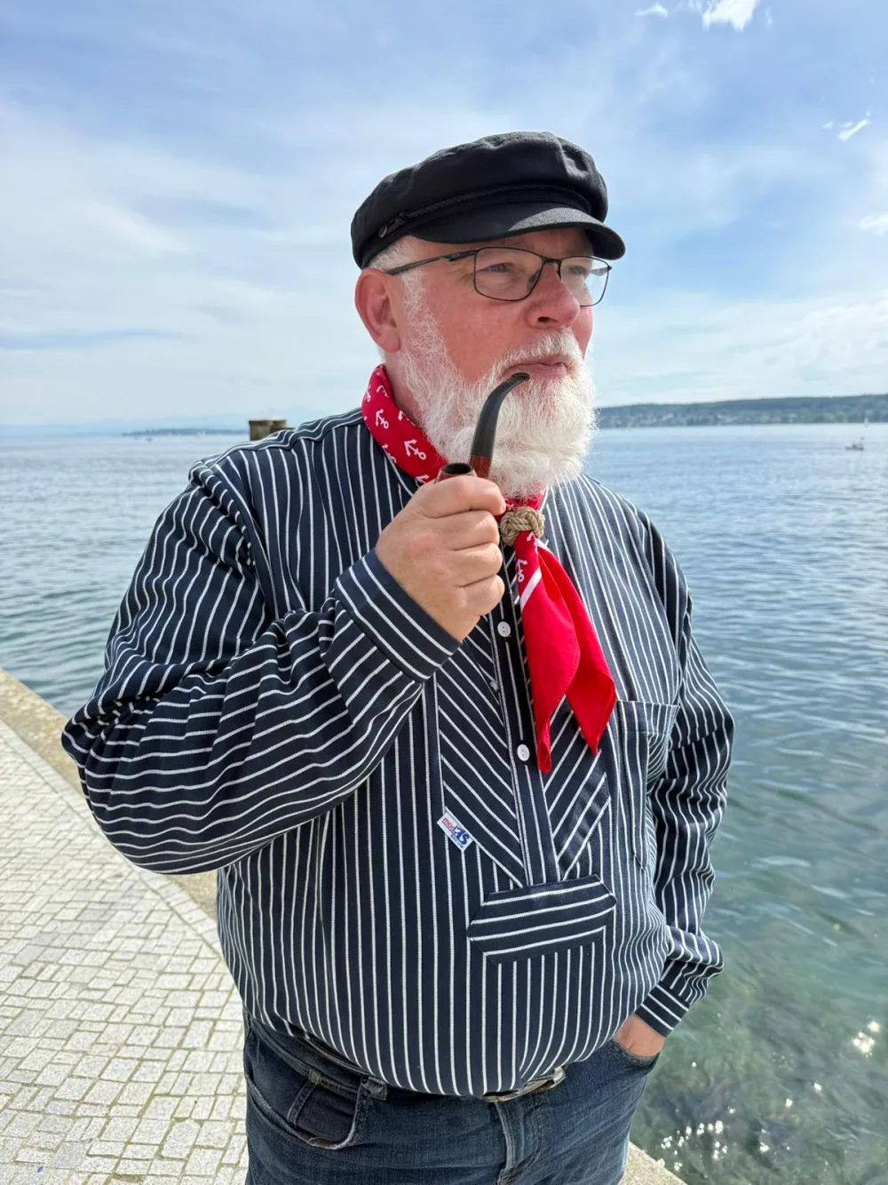 Thomas Drossel mit Kapitänsmütze und Pfeife am Wasser – Inhaber OMNIKUM Yachtservice